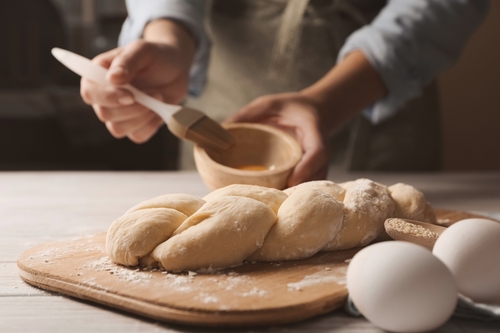 Woman,Spreading,Egg,Yolk,Onto,Raw,Braided,Bread,At,White